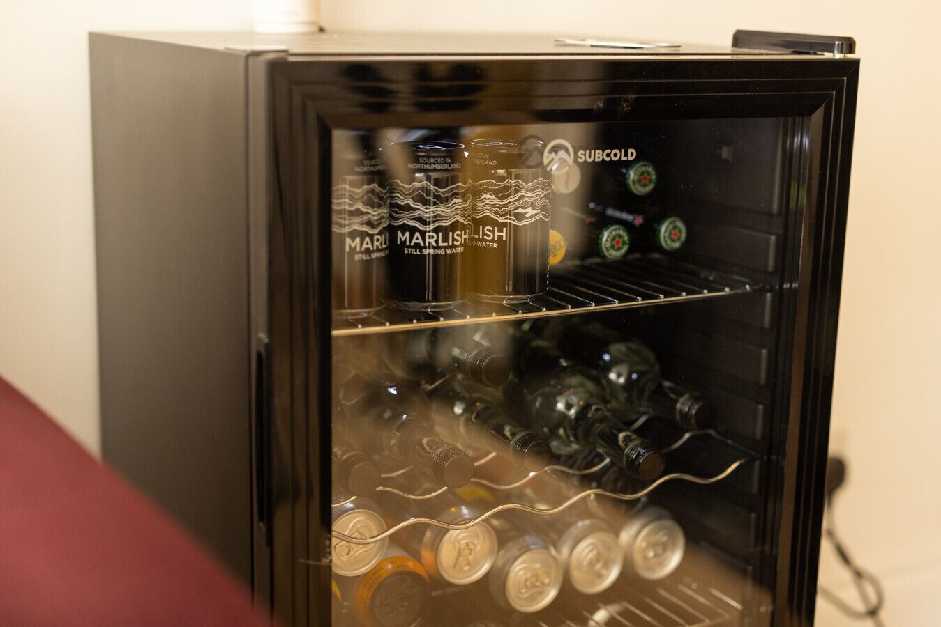 Un réfrigérateur à porte vitrée, contenant diverses boissons et une bouteille étiquetée « Marlish, eau de source naturelle ».