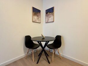 Een kleine kamer met een ronde tafel en twee zwarte stoelen, een klein decoratief object op de tafel, en twee ingelijste foto's aan de muur.
