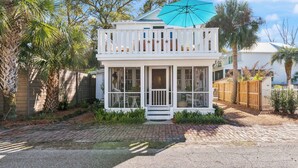 A two-story house with a balcony, a porch, and a large umbrella. - Two Palms Cottage on St Simons (St Simons Island)