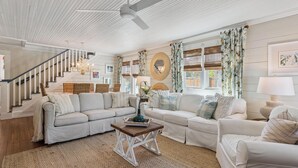 A spacious living room with a staircase, white walls, and a ceiling fan. - Two Palms Cottage on St Simons (St Simons Island)