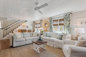 A spacious living room with a staircase, white walls, and a ceiling fan. - Two Palms Cottage on St Simons (St Simons Island)