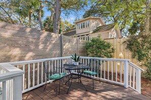 A deck with a white railing, a table with chairs, and a potted plant. - Two Palms Cottage on St Simons (St Simons Island)