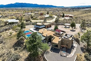 A large, multi-story building with a pool, surrounded by sparse vegetation and distant mountains.