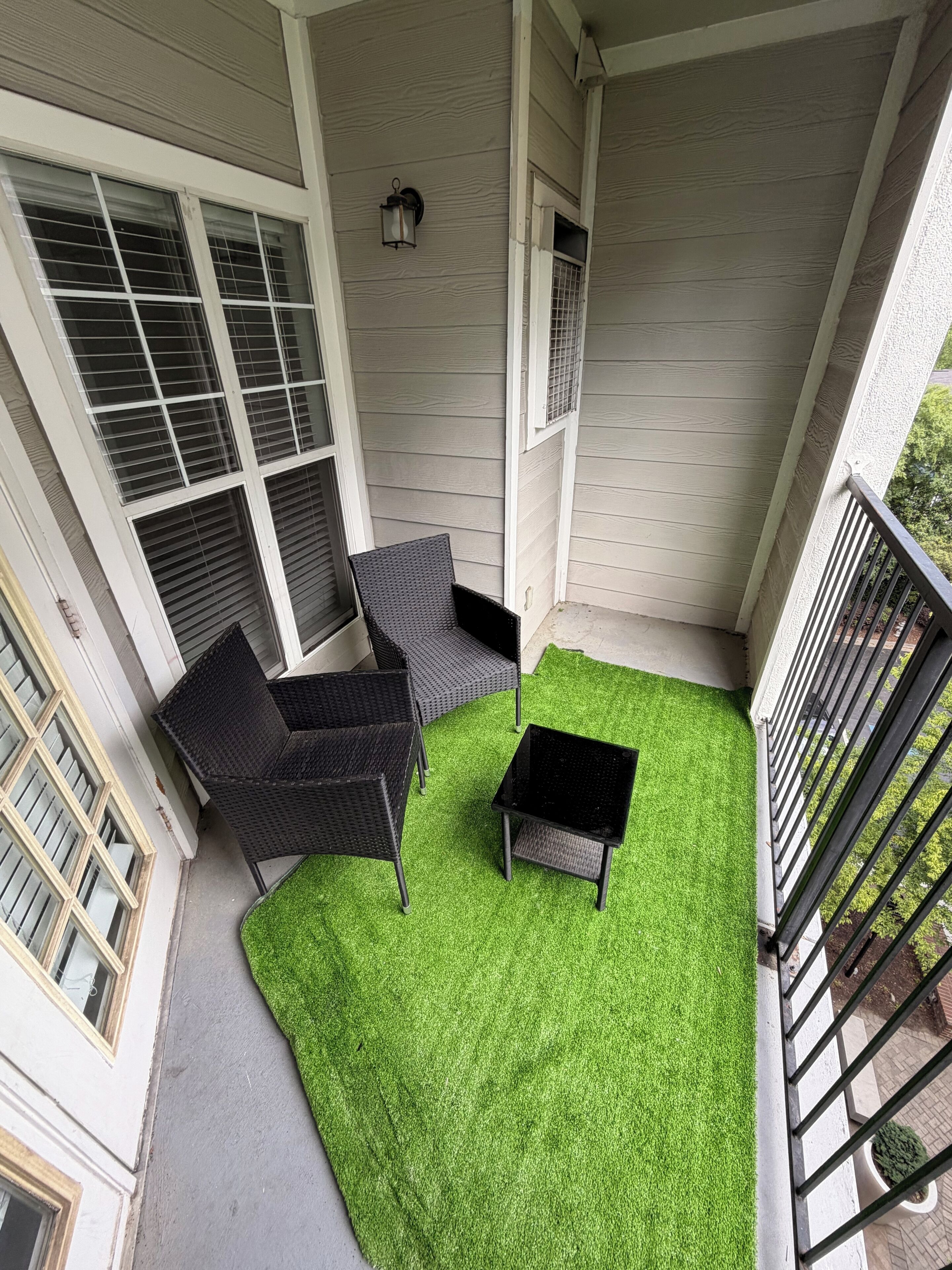 A covered patio with a green artificial turf, a black table, and two wicker chairs.