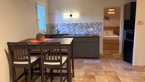A compact kitchen with a dining area, a built-in island, and a small bedroom with a bed and nightstand. - Private Pool • Sillans Waterfall • Verdon • Nature Getaway in Provence (Sillans-la-Cascade)