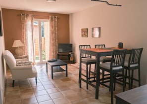 Ein Wohnzimmer mit Fernseher, einem Esstisch mit Stühlen, einer Couch und einem Fenster mit Vorhängen.