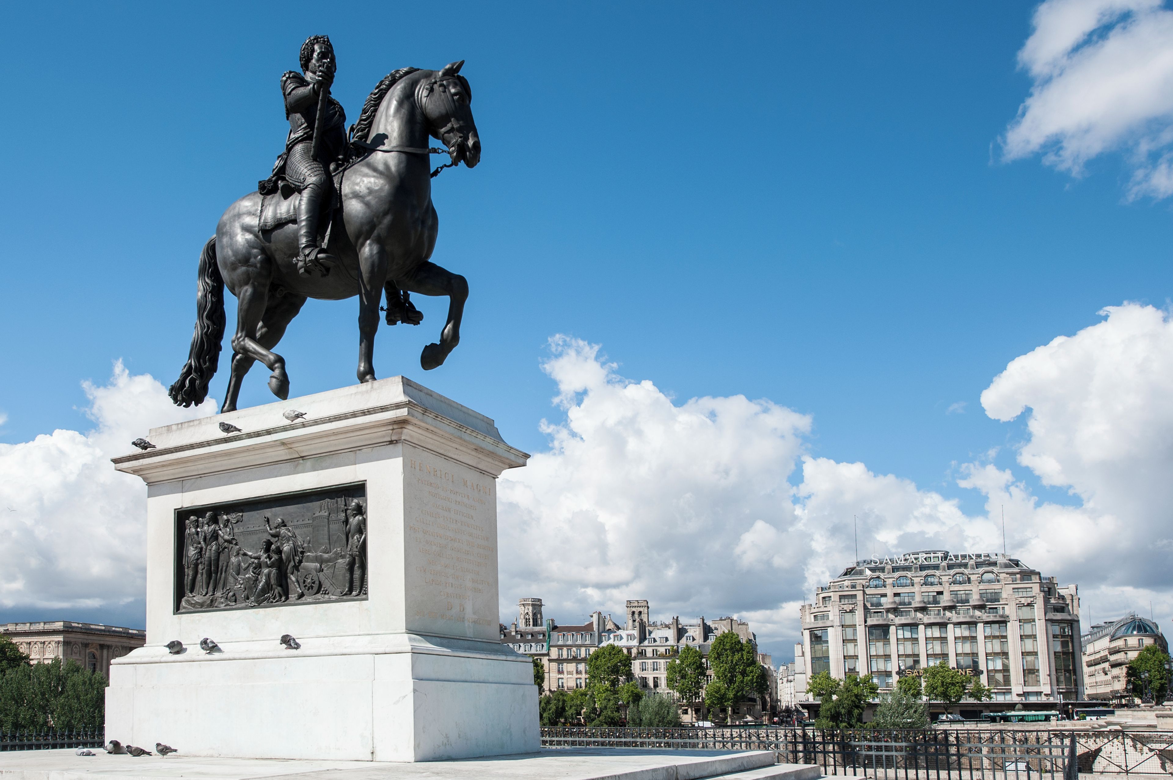 Una statua di un uomo a cavallo, un piedistallo con un rilievo e un edificio sullo sfondo.