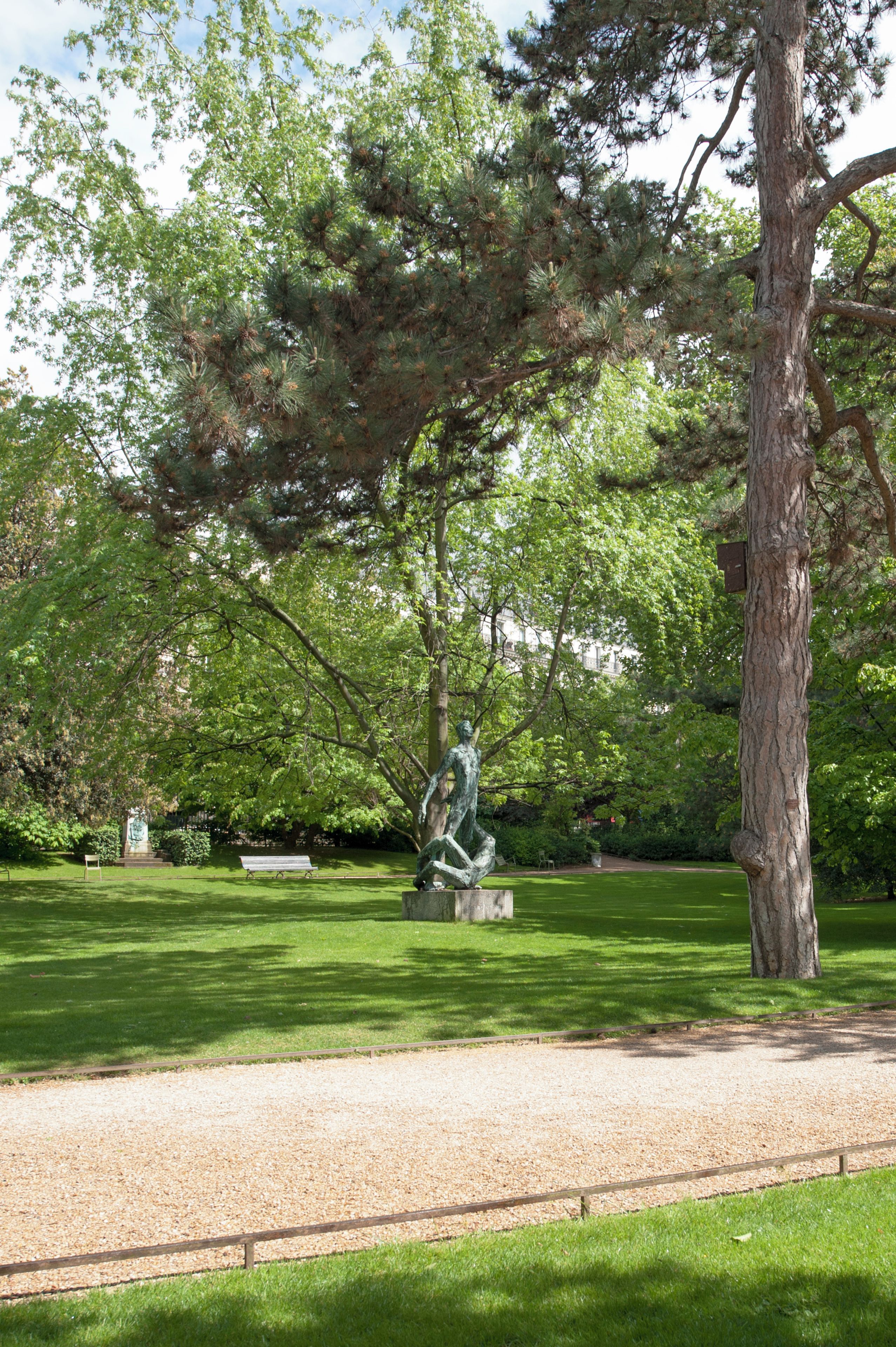Ein Park mit einer Statue, einer Bank und einem Baum.