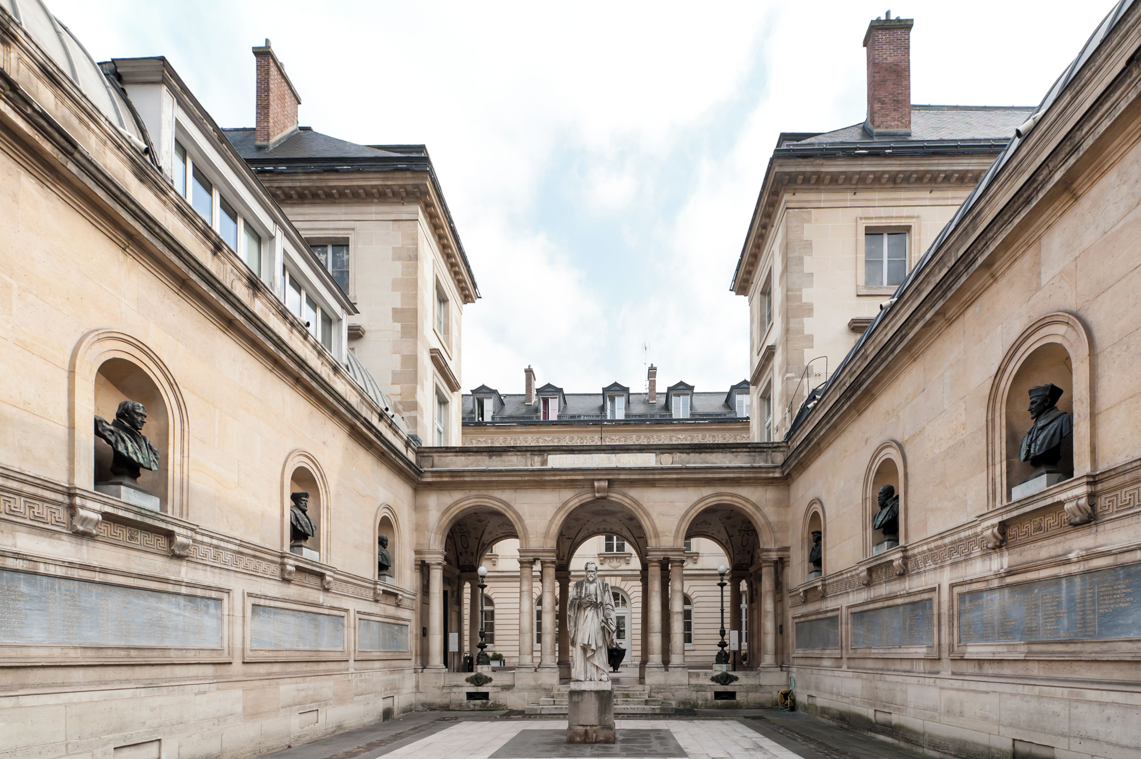 A courtyard with classical architecture, featuring a central statue, arched doorways, and columns.