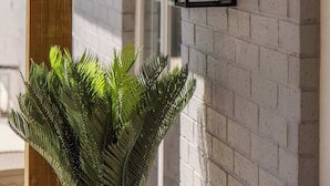 A wall-mounted light fixture with a glass enclosure and a single bulb, a wooden beam structure, and a potted plant. - The Cousins House, private pool, prime location (Rogers)