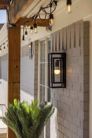 A wall-mounted light fixture with a glass enclosure and a single bulb, a wooden beam structure, and a potted plant. - The Cousins House, private pool, prime location (Rogers)