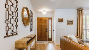 A hallway with a wooden bench, a wooden door, a brown leather sofa, and a wall-mounted mirror. - The Cousins House, private pool, prime location (Rogers)