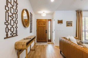 A hallway with a wooden bench, a wooden door, a brown leather sofa, and a wall-mounted mirror. - The Cousins House, private pool, prime location (Rogers)