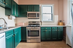 A kitchen with teal cabinets, a stainless steel stove, a microwave, and a window. - Jan 2027 open ! A-ville Historic Apt w/ Office (Chicago)