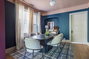 A dining area with a dark table, six chairs, a plaid rug, a window with curtains, and a door. - Jan 2027 open ! A-ville Historic Apt w/ Office (Chicago)