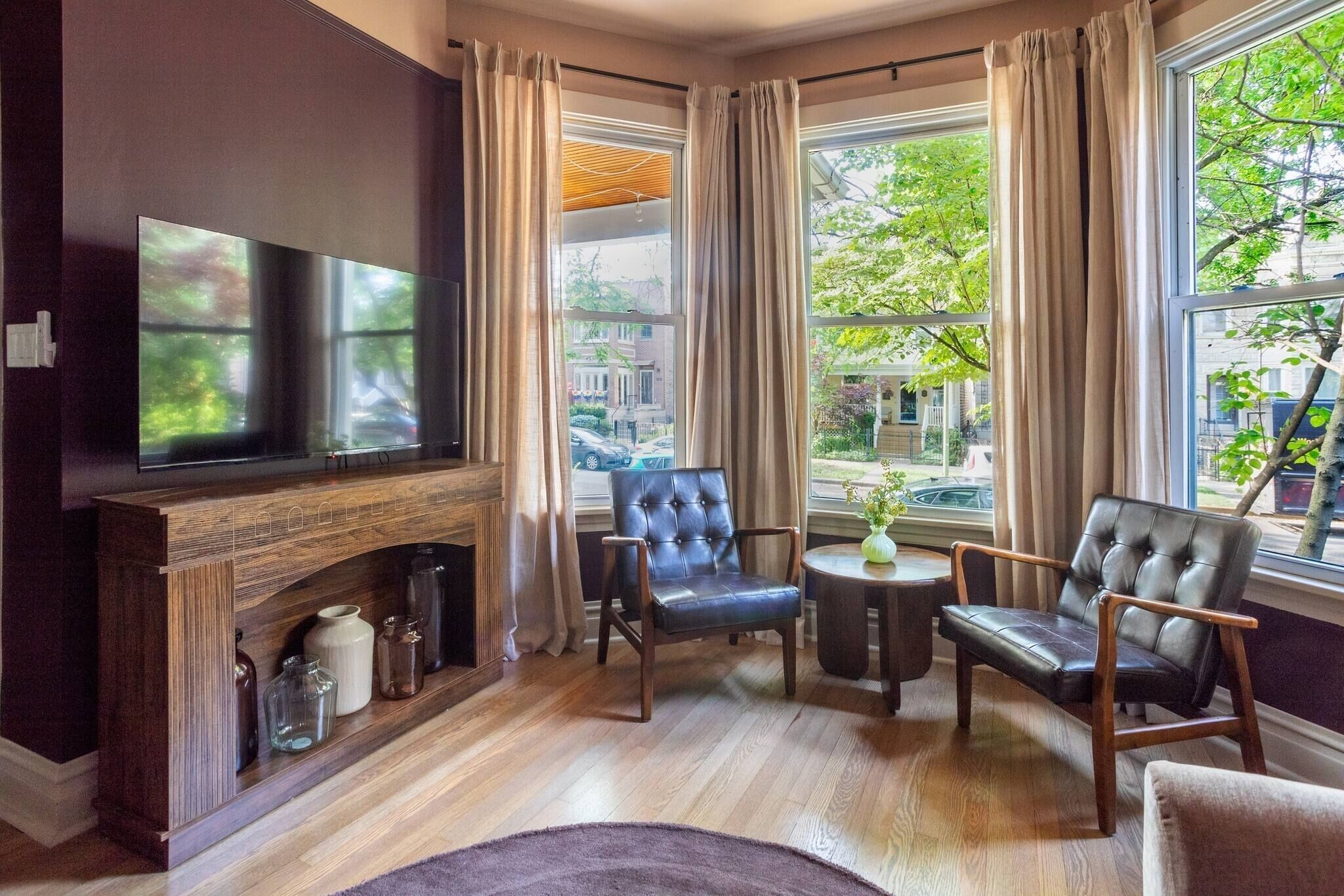Una sala de estar moderna con un televisor de pantalla plana, sillones de cuero, chimenea y ventanas amplias con cortinas.