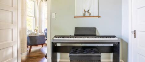 A piano in a hallway with a bench, a chair, and a wall-mounted picture.