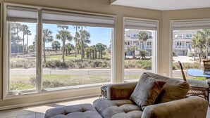 A room with large windows, a sofa, and a dining table. - Seabrook Exclusives | 702 Spinnaker Beach (Seabrook Island)