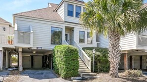A two-story house with a covered garage, a staircase, and a palm tree. - Seabrook Exclusives | 702 Spinnaker Beach (Seabrook Island)
