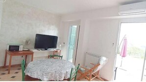 Ein Zimmer mit einem Bett, einem Tisch mit Fernseher, einem Stuhl, einer Heizung und einem Balkon mit einem rosa Sonnenschirm.