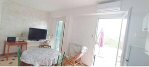 Ein Zimmer mit einem Bett, einem Tisch mit Fernseher, einem Stuhl, einer Heizung und einem Balkon mit einem rosa Sonnenschirm.