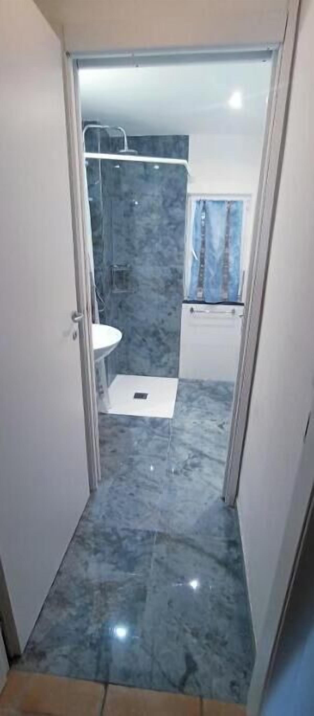 Ein schmaler Gang führt zu einem Badezimmer mit einem weißen Waschbecken und einer Duschkabine.