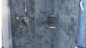 Eine Dusche mit Handbrause und Wandarmatur, einer Glastür sowie einem weißen Waschbecken inklusive Armatur.