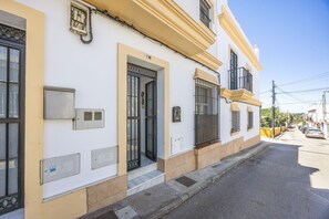 Ein weißes Gebäude mit gelber Fassade, Nummer 7B, mit einer Metalldür, vergitterten Fenstern und einem kleinen Balkon.
