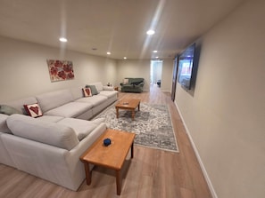 Uma sala de estar com sofá, duas mesas de centro, tapete e televisão na parede.