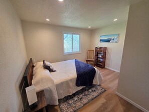 Quarto com cama, janela, cadeira, estante de livros e um quadro na parede.