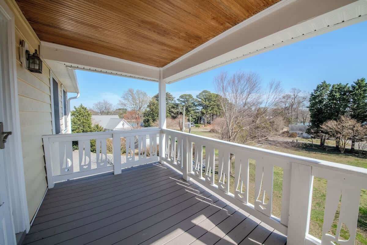 A covered porch with a wooden ceiling, white railings, and a view of a residential area with trees and houses.