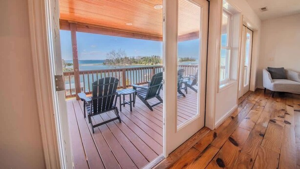 Una habitación con piso de madera, puerta corrediza de vidrio que da a una terraza con mobiliario exterior y vista al océano.