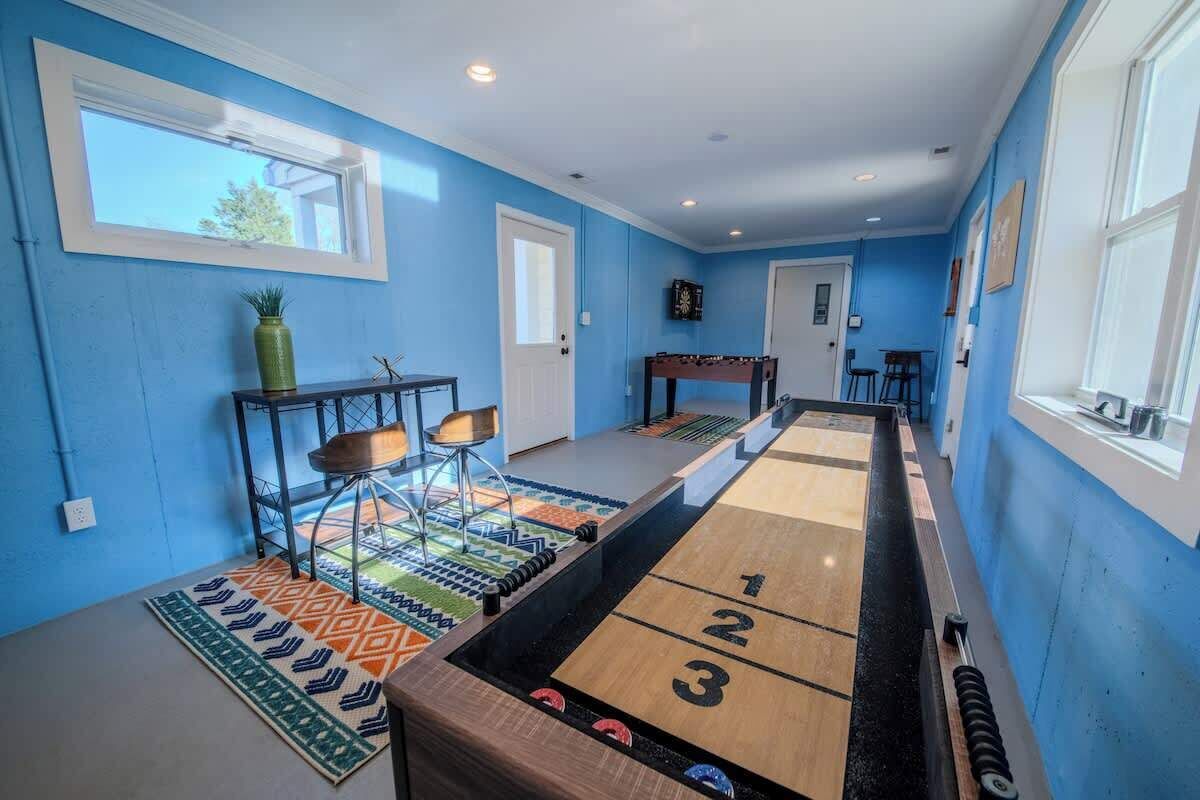 Una stanza con tavolo da shuffleboard, un piccolo tavolo con sedie e una finestra con persiane.