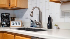 A kitchen with a stainless steel faucet, a coffee maker, and a sign that reads 'COFFEE'.