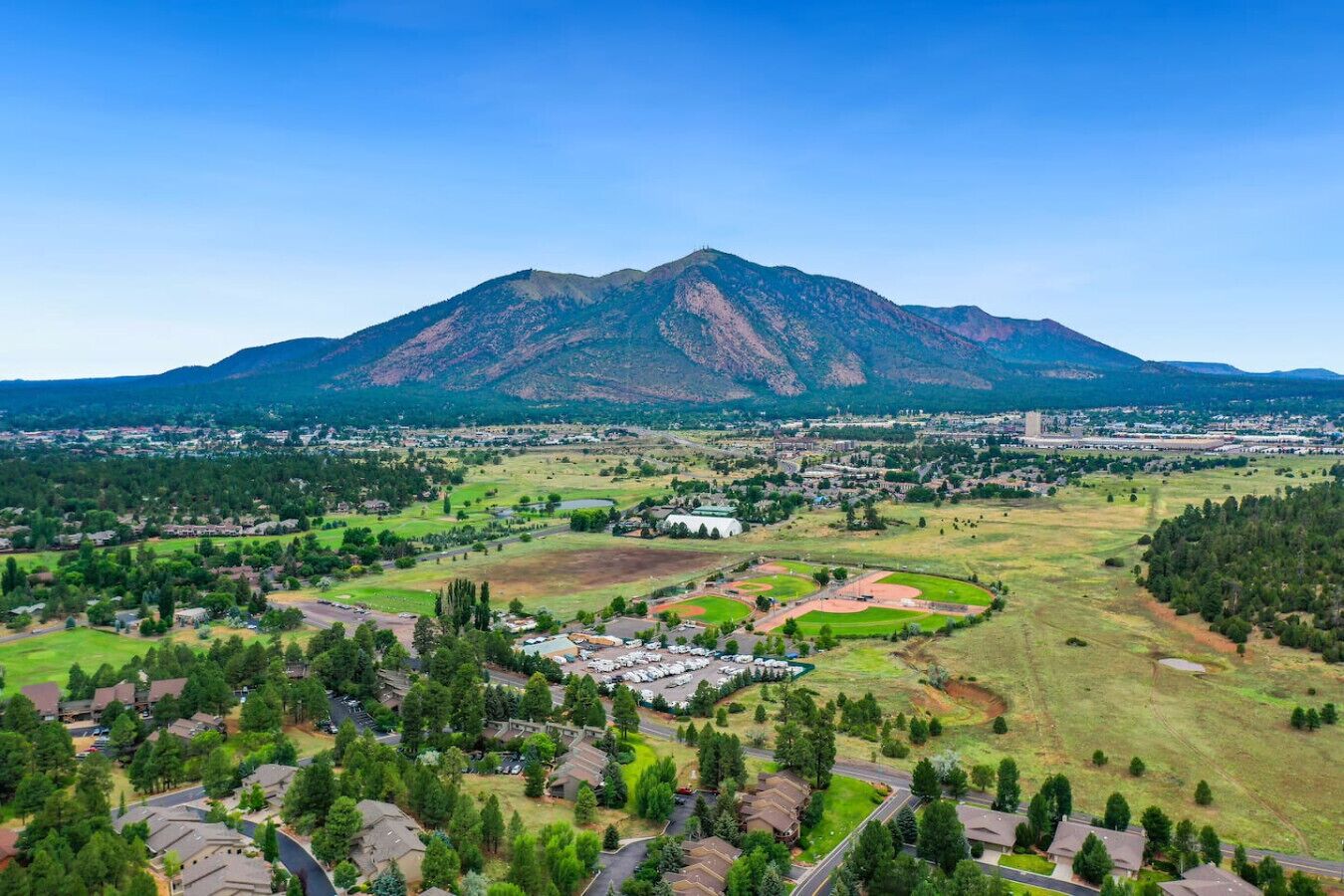 A residential area with houses, a baseball field, and a mountain in the background.