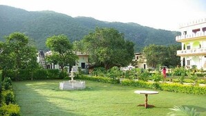 A garden with a fountain, trees, and buildings in the background. - Hotel Pushkar Heritage (Pushkar)