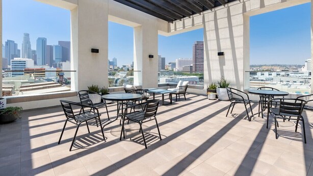 A rooftop terrace with outdoor seating, large windows, and a city skyline view.