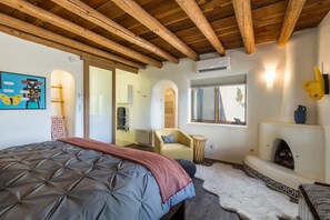 A bedroom with a bed, a fireplace, a window, and a wooden ceiling.