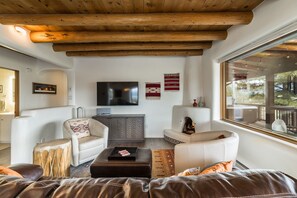 A modern living room with a fireplace, a flat-screen TV, and a large window offering a view of the outdoors.