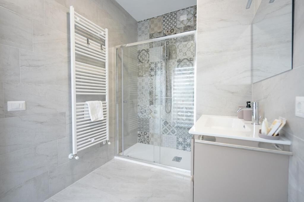 A modern bathroom with a glass shower enclosure, a white sink, and a tiled shower wall.