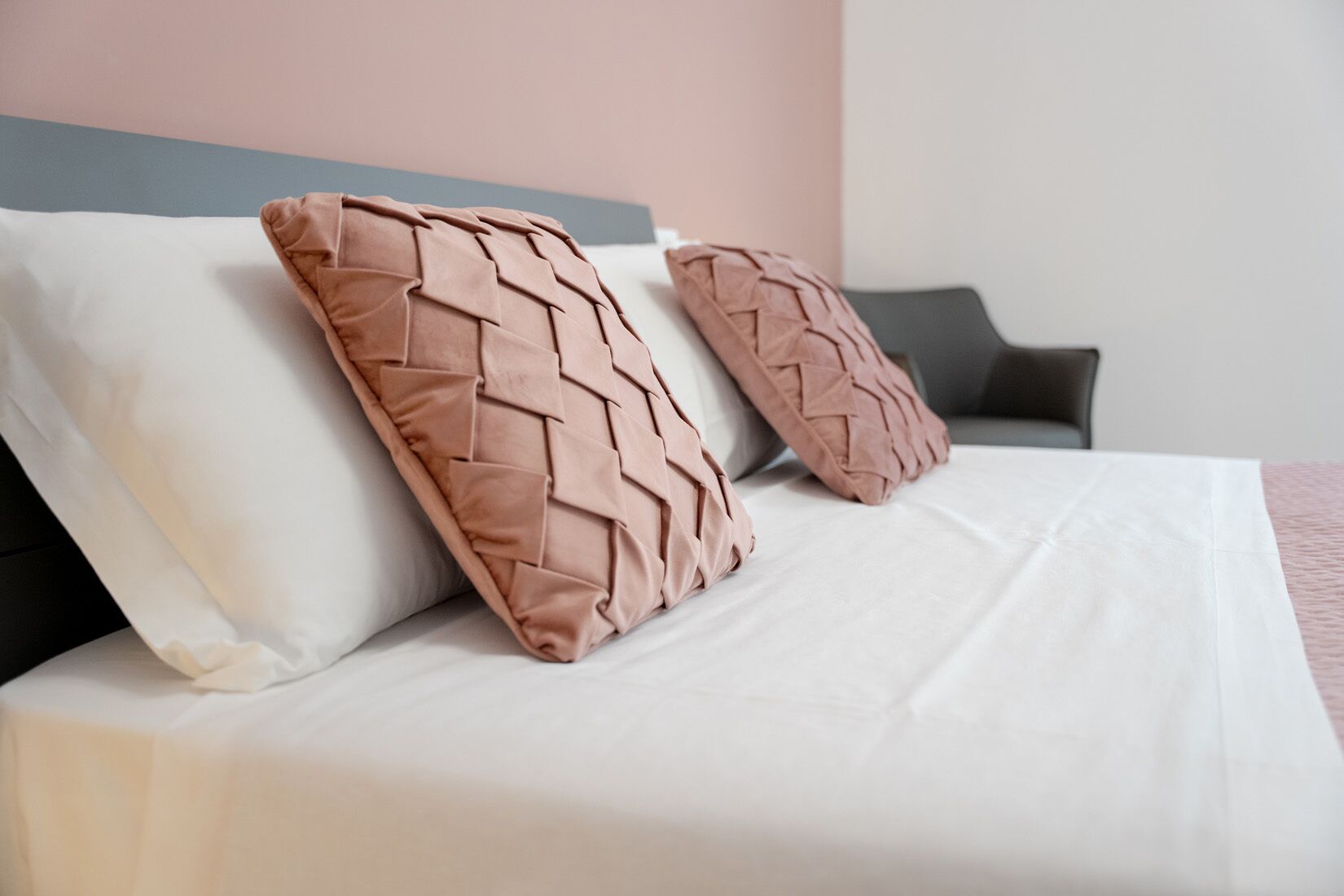 A bed with white bedding and two textured pillows.