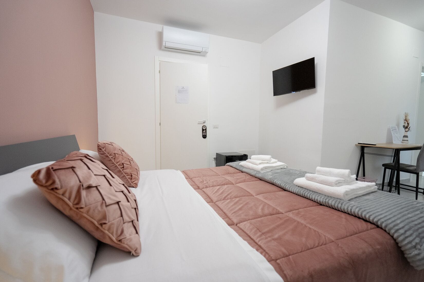 Habitación de hotel con cama, escritorio, silla, televisor y aire acondicionado.