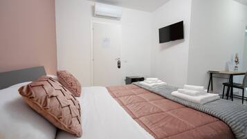 Habitación de hotel con cama, escritorio, silla, televisor y aire acondicionado.