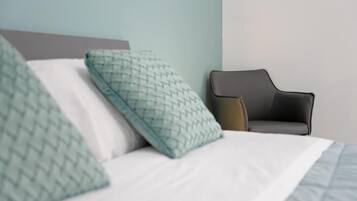 A bed with patterned pillows, a grey chair, and a plain wall.