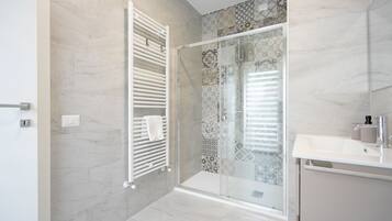 Un bagno moderno con cabina doccia in vetro, un asciugamano bianco sul termosifone e un lavandino bianco con specchio.