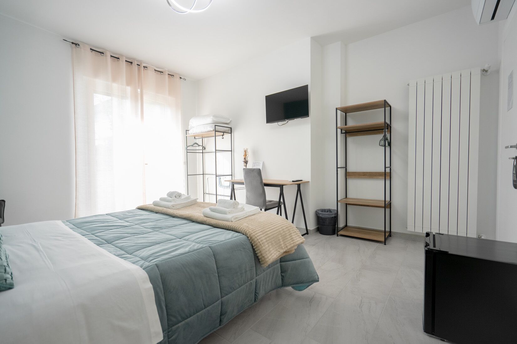 A modern hotel room with a bed, a desk, a TV, and a wardrobe.