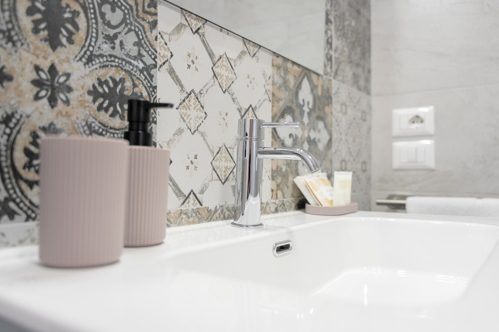 Un bagno con un lavandino bianco, un rubinetto moderno e piastrelle decorate sulle pareti.