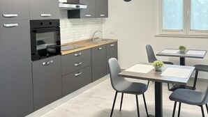 Une cuisine moderne avec des meubles gris, un four encastré et un coin repas comprenant une table et des chaises.