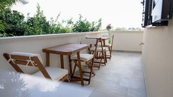 Una terraza con mesas y sillas de madera, una planta en maceta y vistas al verdor.