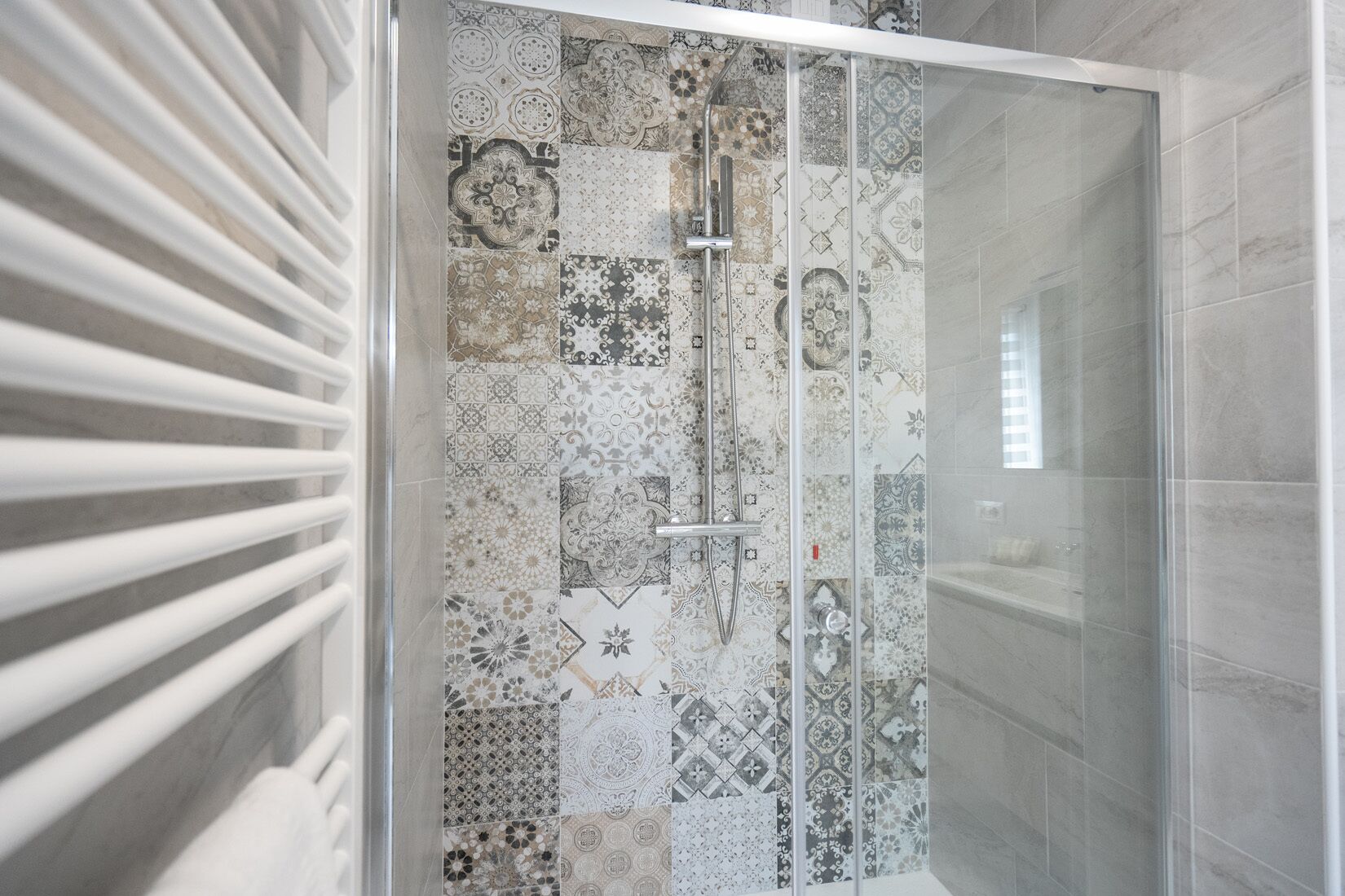 Una doccia con porta in vetro, pareti piastrellate con diversi motivi e soffitto bianco.